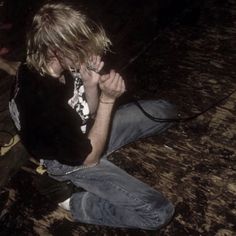 a young man sitting on the floor talking on a cell phone with his hand in his mouth