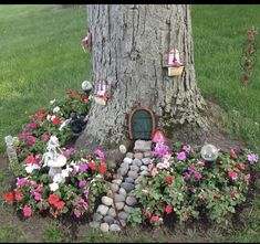 there is a tree with flowers around it and a gnome's house in the middle