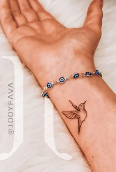 a woman's arm with a tattoo on it and a hummingbird charm attached to the wrist