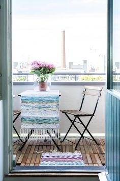 two chairs and a table on a balcony with flowers in the potted planter