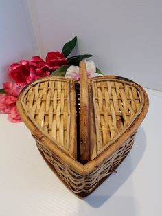 a heart shaped basket sitting on top of a white table next to red and pink flowers