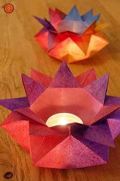 three paper flowers sitting on top of a wooden table next to a lit candle holder