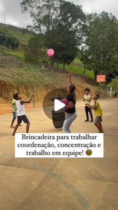 children are playing with a ball in an open area near a hill and some trees