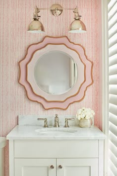 the bathroom is decorated in pink and white with gold accents on the mirror above the sink