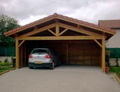 a car is parked in front of a wooden garage with an attached carport and roof