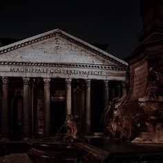 an old building with columns in front of it and a fountain at the base that is lit up