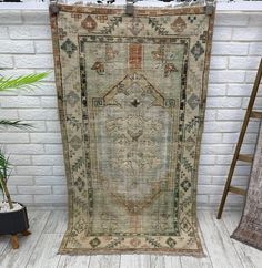 an antique rug is displayed in front of a white brick wall and potted plant