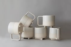 several white cups and mugs stacked on top of each other in front of a gray background