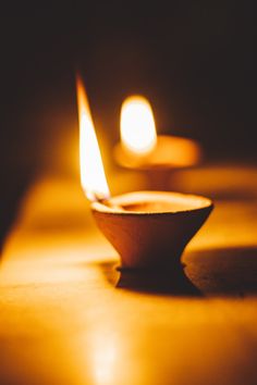 two lit candles sitting on top of a wooden table next to each other in the dark