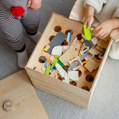 a child playing with legos in a wooden box on the floor next to other toys