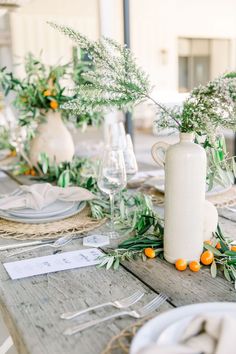 the table is set with oranges and greenery in white vases on it