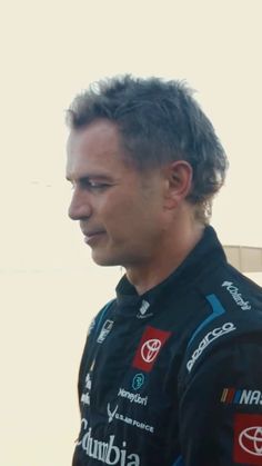 a man standing in front of a building wearing a black suit and red shirt with logos on it