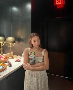 a woman standing in front of a counter with food on it and an exit sign behind her