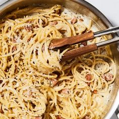 a pan filled with pasta and meats on top of a stove next to two wooden utensils