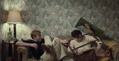 two boys sitting on a couch reading books in front of a wallpapered background