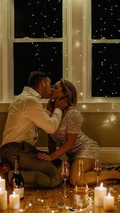 a man and woman sitting on the floor in front of a window with lit candles