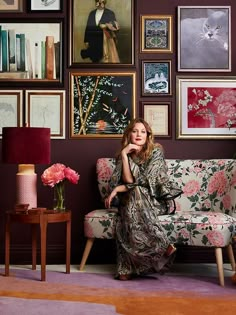 a woman sitting on top of a couch in front of a wall full of pictures