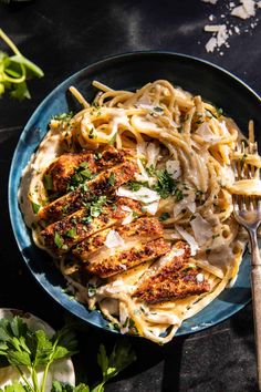 a plate of pasta with chicken and parmesan cheese on top, garnished with parsley