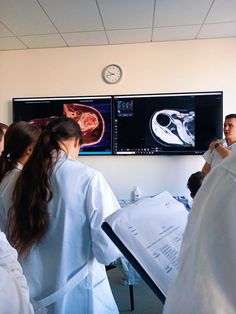 some people in white lab coats are looking at mri images on the wall behind them