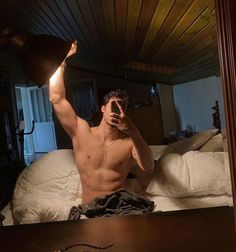 a shirtless man sitting on top of a bed while holding a lamp up to his face