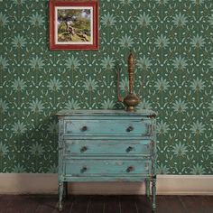 an old dresser in front of a green wallpaper with a painting on the wall