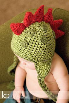 a baby wearing a green crocheted hat with red horns on it's head