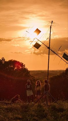 three people are standing in the grass near a radio antenna and some trees at sunset