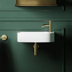 a white sink sitting next to a green wall with brass fixtures on the faucet