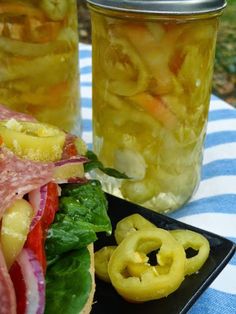 a sandwich on a plate with pickles next to it and two jars full of pickles