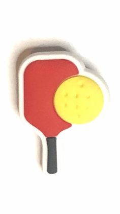 a red and yellow paddle shaped object on a white surface with a black stick sticking out of it