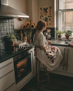 a woman sitting on a stool in a kitchen next to an oven with sunflowers