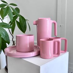 pink coffee cups and mugs are sitting on a white table next to a potted plant