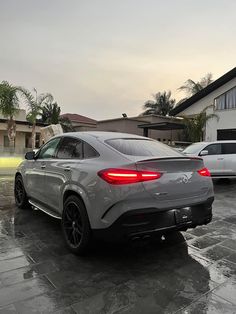 the rear end of a silver mercedes suv parked in front of a house on a rainy day