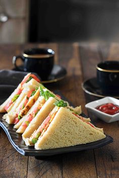 a sandwich cut in half sitting on top of a black plate next to a cup of coffee