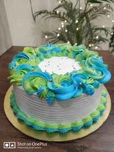 a cake with blue and green frosting on a table next to a potted plant