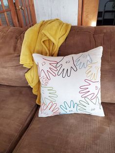 a brown couch with a yellow blanket on top of it next to a pillow that has colorful writing on it