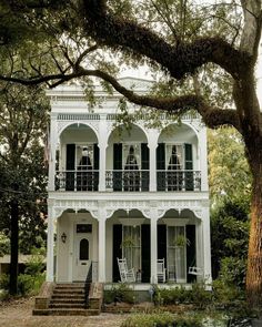 an old white house with black shutters and balconies on the second story