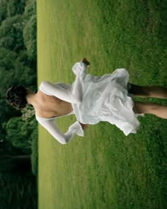 a woman in a white dress standing on top of a lush green field