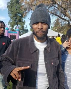 a man wearing a beanie pointing to the side while standing in front of other people