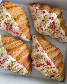 four croissants with white frosting and sprinkles in a box