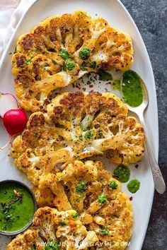 cauliflower with pesto sauce on a white platter next to a spoon