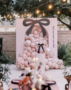 an outdoor party with balloons and lights on the tree branches, decorated in pink tones