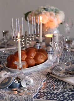 a table topped with plates and candles next to other place settings on top of a cloth covered table