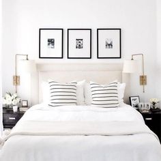 a white bed topped with pillows and two framed pictures on the wall above it's headboard