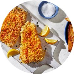 two fish fillets on a cutting board with lemons and seasoning next to them