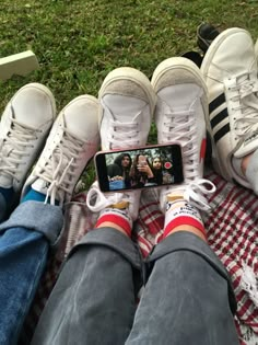 two people sitting on a blanket with their feet crossed and one person holding a cell phone