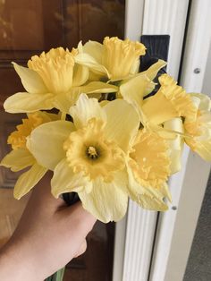 a hand holding a bunch of yellow flowers in front of a door way with a handle