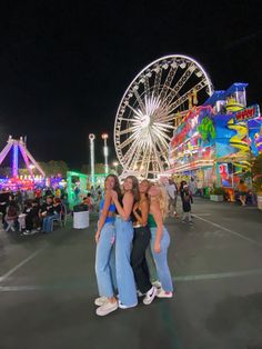 three girls hugging each other in front of a ferris wheel