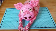 a pink stuffed pig laying on top of a cutting board next to a pair of scissors