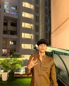 a man standing in front of a building with his hand up to the camera and palm trees behind him